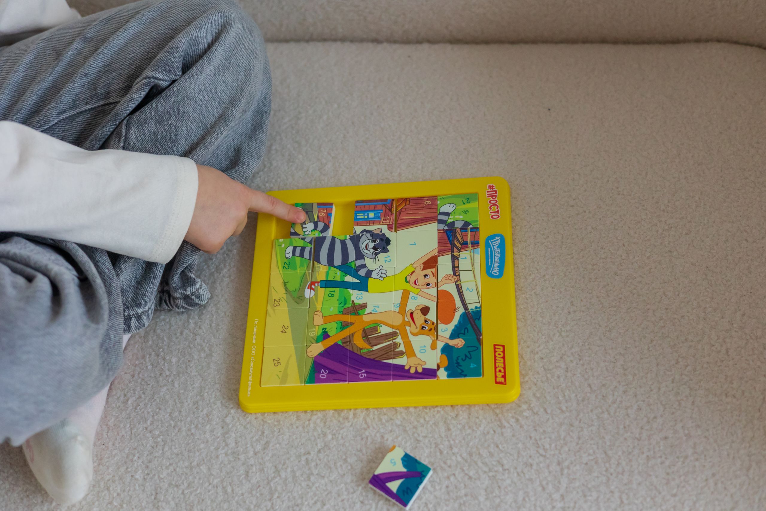 Ein kleines Kind beschäftigt sich drinnen auf einem gemütlichen Teppich mit einem bunten Cartoon-Puzzle.