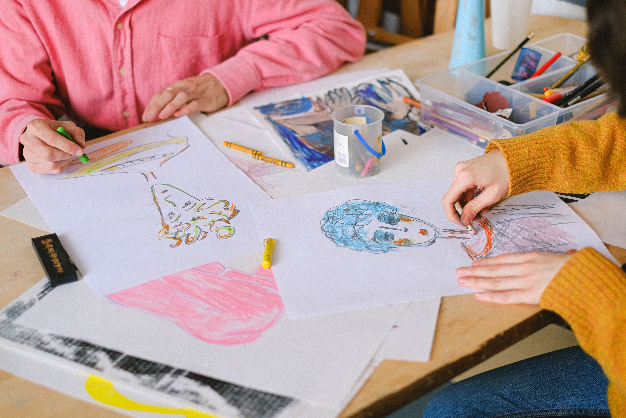 Von oben: Talentierte Künstler zeichnen Bilder mit bunten Buntstiften, während sie am Tisch sitzen und im Kunstatelier Gemälde schaffen