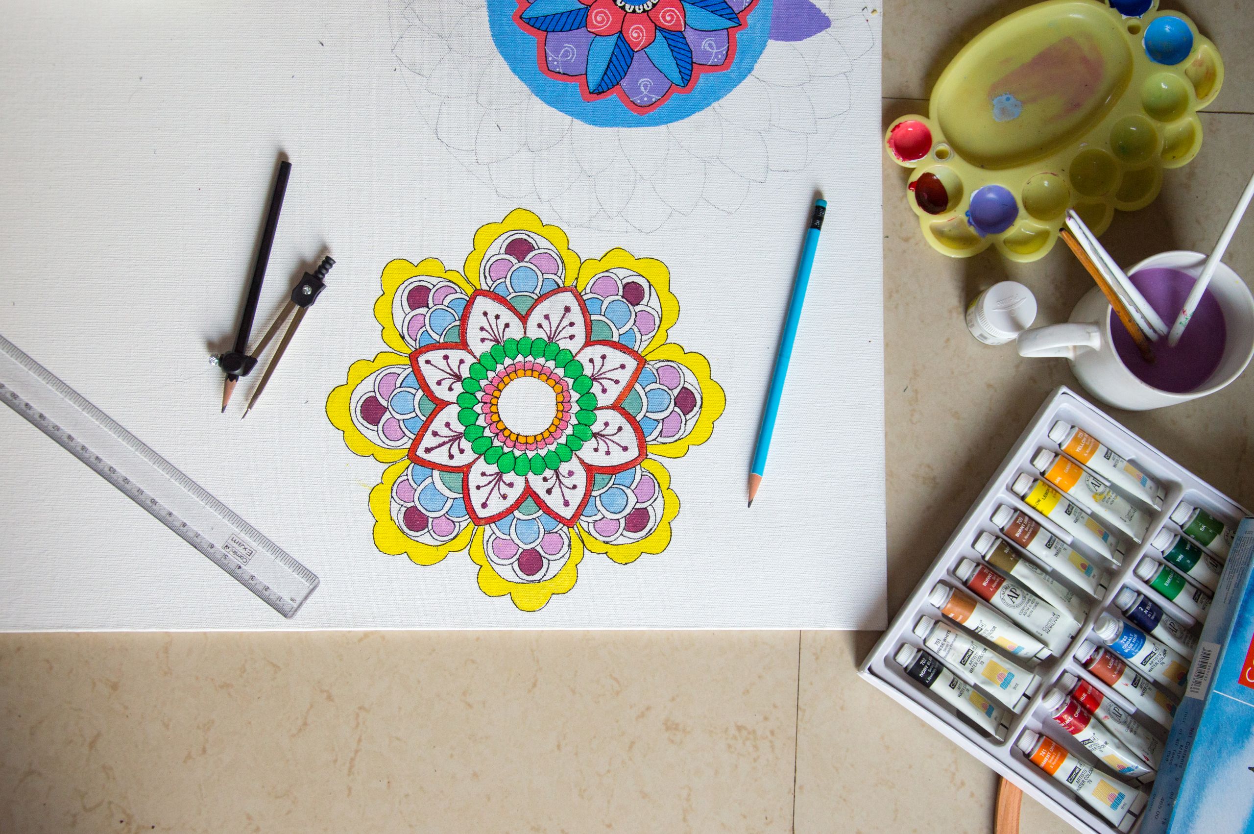 Vibrant mandala drawing with pencils, paint, and tools arranged neatly on a workspace.
