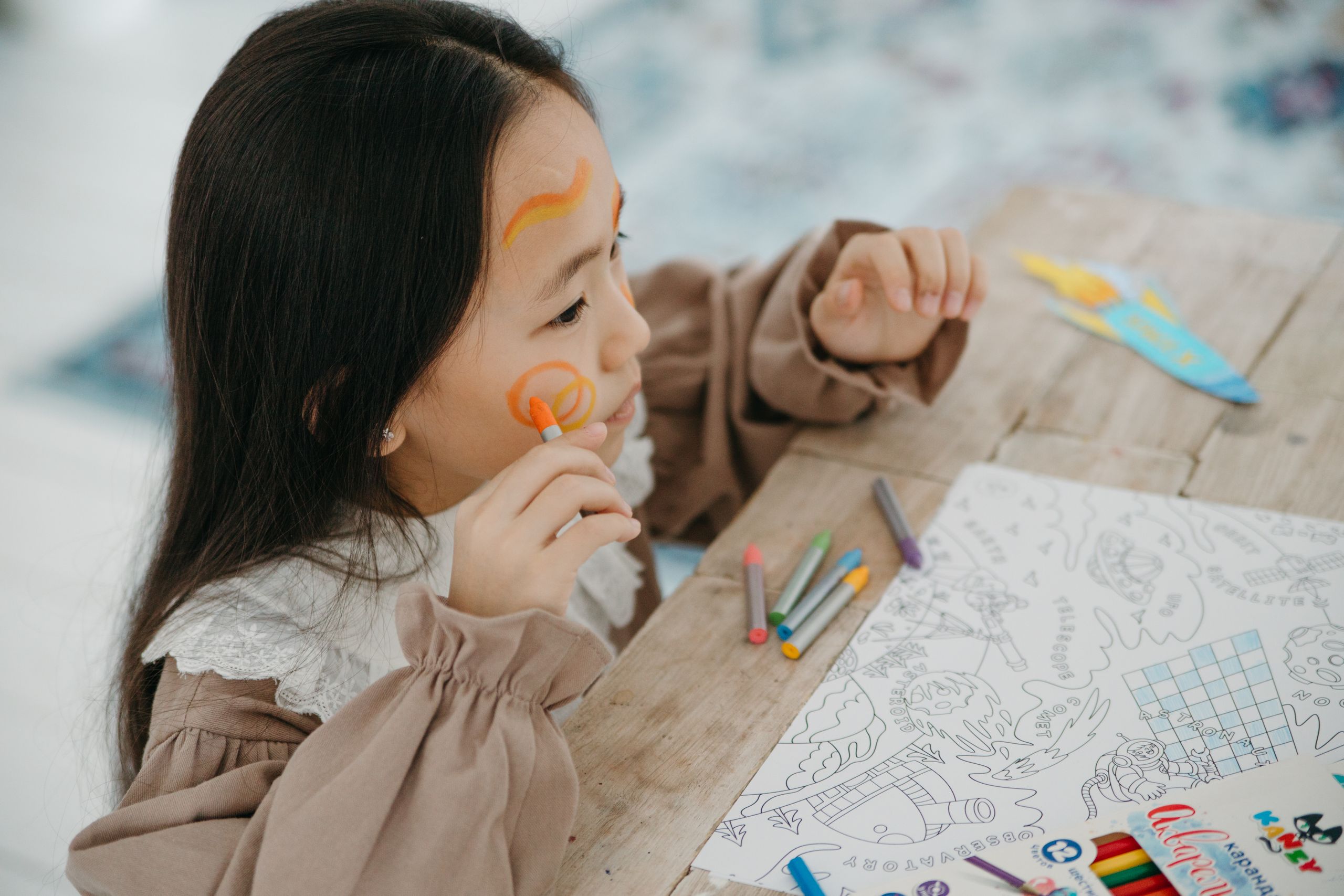 Niña divirtiéndose pintando caras y dibujando, expresando creatividad y alegría.